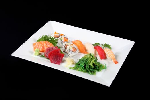 sushi and sashimi with wasabi and vegetable in white plate on a black background