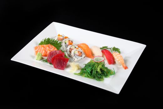 sushi and sashimi with wasabi and verrdura in white plate on a black background