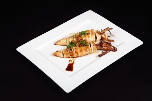 grilled squid with decoration of vegetables in white plate on a black background