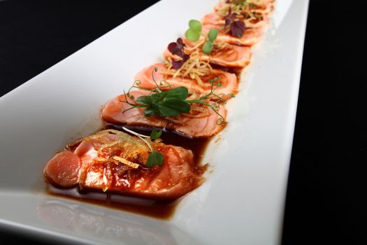 close-up salmon meat with sauce in white dish on black background