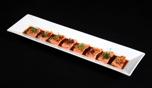 Salmon meat with sauce in white dish on black background