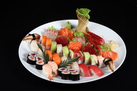 sushi and sashimi mixed on round white plate on a black background