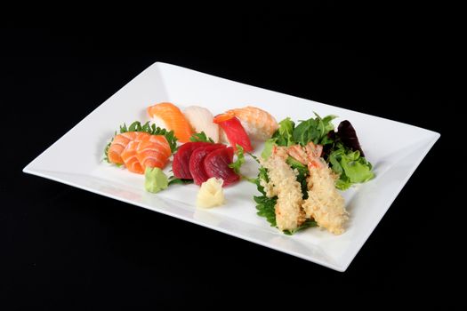 sushi and sashimi with wasabi and vegetable in white plate on a black background