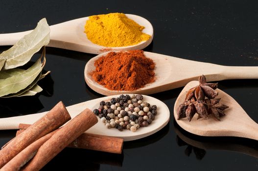 Wooden spoons filled with spices on black background