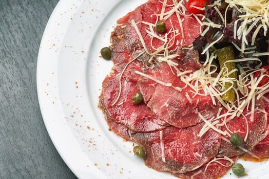 Carpaccio with olives and Parmesan on white plate
