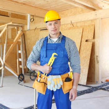Workman with wrench inside wooden house under construction