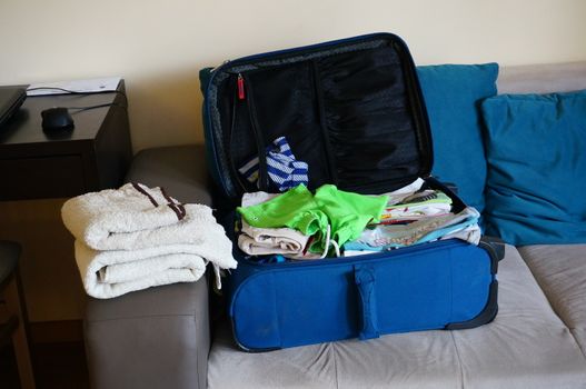 Blue suitcase full of clothes lying on sofa