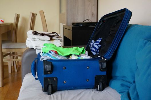 Blue suitcase full of clothes lying on sofa