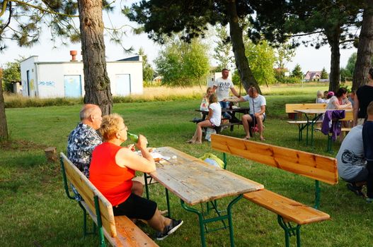 SIANOZETY, POLAND - JULY 22, 2015: People sitting on benches by wooden tables on a barbecue event