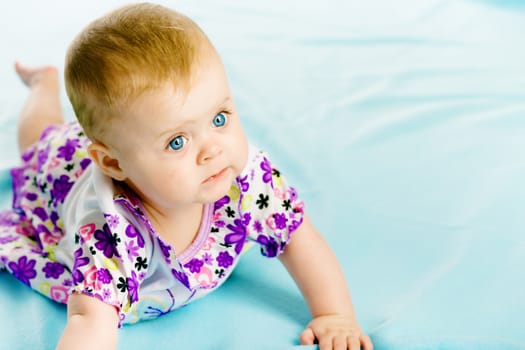 blue-eyed baby girl in a dress creeps on the blue coverlet
