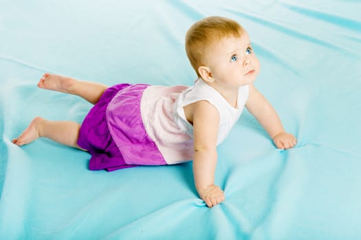 blue-eyed baby girl in a dress creeps on the blue coverlet