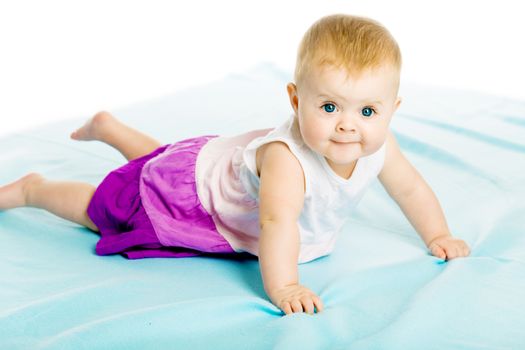 blue-eyed baby girl in a dress creeps on the blue coverlet