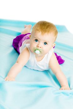blue-eyed baby girl with pacifier crawling on the blue coverlet
