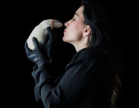 Brunette woman in black standing in front of a black backdrop, holding a white dumbo rat, looking at it with affection and love.