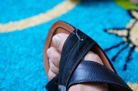 Foot in leather sandal on blue carpet