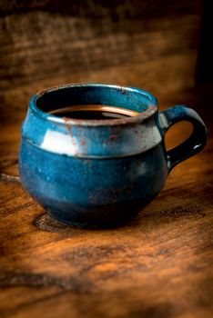 Coffee in grunge blue clay cup on rustic wooden background