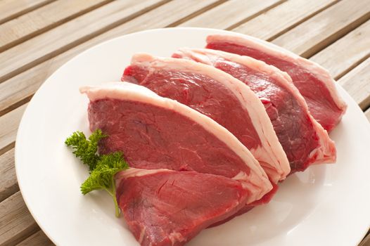 Four fresh raw tender beef steaks with a fatty rind arranged on a plate with parsley ready for cooking