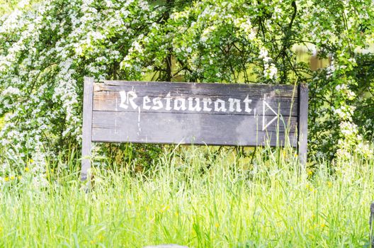 Information Sign of weathered wood with inscription Restaurant. In the background of green trees.