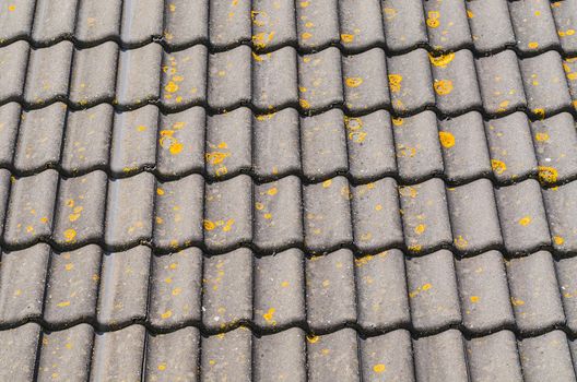 Detail some old house roof with mossy and weathered roof tiles.