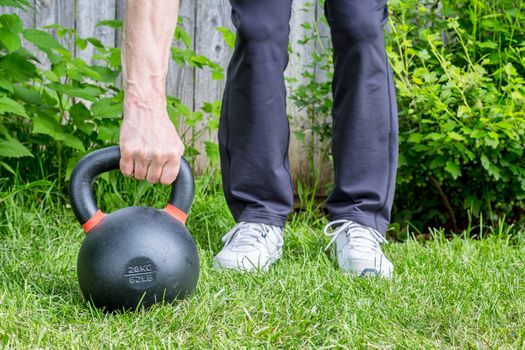 outdoor fitness concept - weight training with a heavy iron competition kettlebell (62lb/28 kg) on green grass in backyard