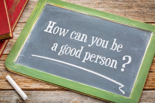 How can you be a good person? An inspirational question on a  blackboard with a white chalk and books against rustic wooden table