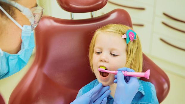 Little patient at the dentist office. The dentist brushes teeth to the little girl