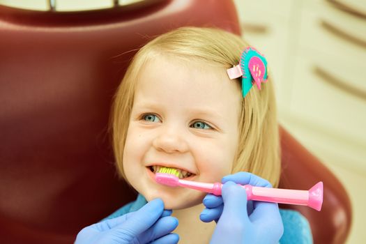 Little girl sitting in the dentists office. The dentist brushes teeth to the little girl