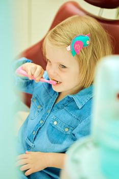 Little girl sitting in the dentists office brushes teeth