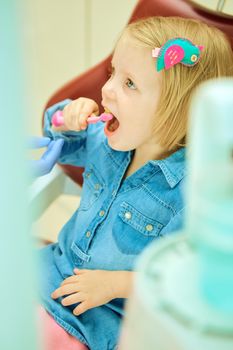 Little girl sitting in the dentists office brushes teeth