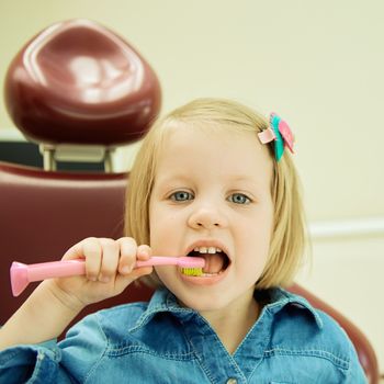 Little girl sitting in the dentists office brushes teeth