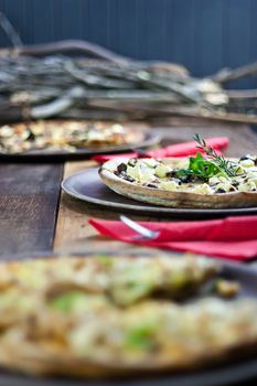 Three pizzas laid out on wooden trays on a rustic wooden table in a pizzeria.