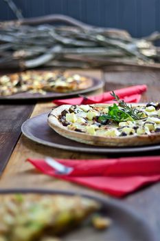 Three pizzas laid out on wooden trays on a wooden tables in a pizzeria.