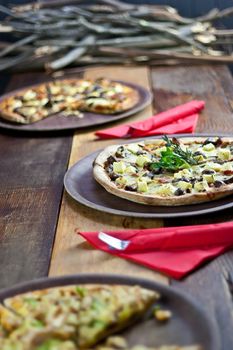 Three pizzas laid out on wooden trays on a wooden tables in a pizzeria.