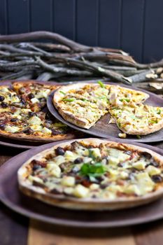 Three pizzas laid out on wooden trays on a wooden tables in a pizzeria.