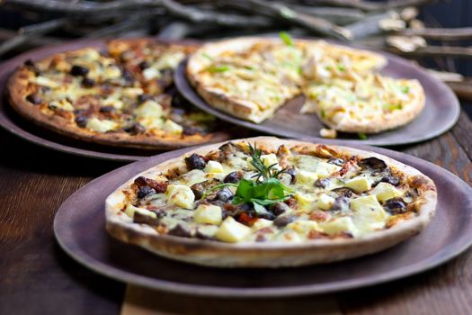 Three pizzas laid out on wooden trays on a wooden tables in a pizzeria.