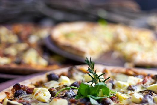 Three pizzas laid out on wooden trays on a wooden tables in a pizzeria.