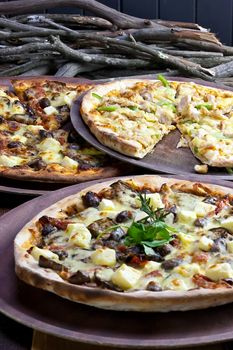 Three pizzas laid out on wooden trays on a wooden tables in a pizzeria.