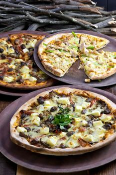 Three pizzas laid out on wooden trays on a wooden tables in a pizzeria.