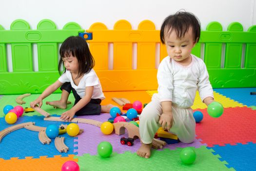 Two Asian Chinese little girls playing with blocks and toys train on the floor at kingdergarten.