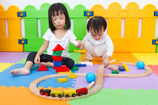 Two Asian Chinese little girls playing with blocks and toys train on the floor at kingdergarten.