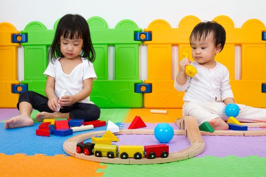 Two Asian Chinese little girls playing with blocks and toys train on the floor at kingdergarten.