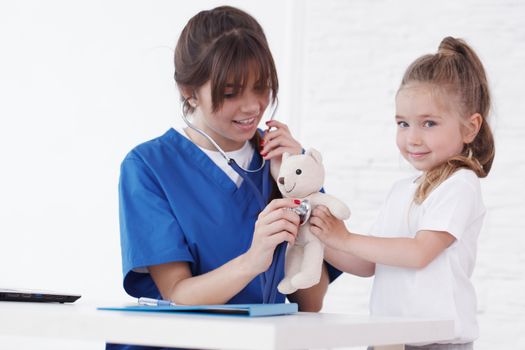 Young smiling female doctor and her little patient with teddy bear