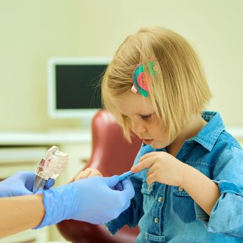 Little girl sitting in the dentists office learning to clean teeth