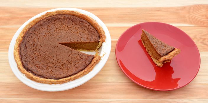 Homemade pumpkin pie with a slice served on a red plate on a wooden table