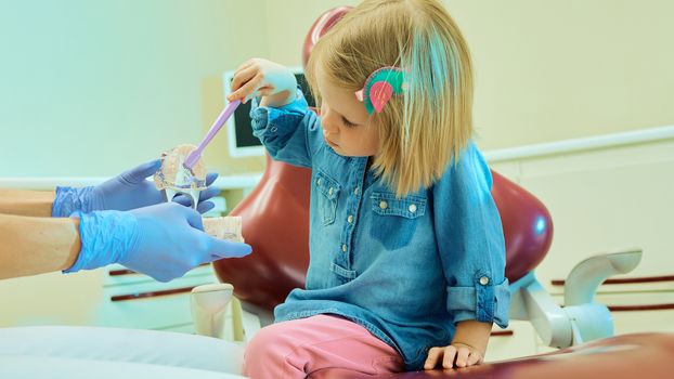 Little girl sitting in the dentists office learning to clean teeth