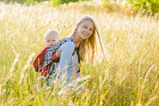 Young mother with her daughter resting in a sunny afternoon in a meadow surrounded by golden light and high grass