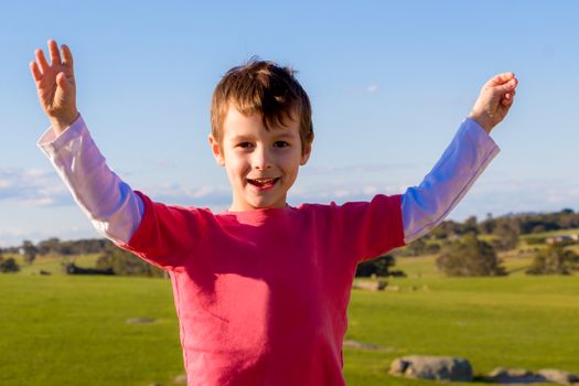 Happy boy with arms up standing in a green field.