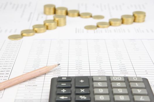 Brown pencil have blur calculator as foreground and blur step of gold coins on finance account as background.