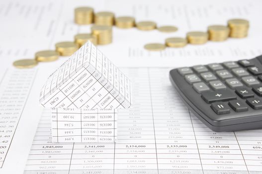 House with calculator have blur step of gold coins on finance account as background.