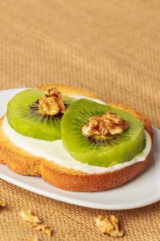 Toast with kiwi, cheese and walnuts on a piece of sackcloth with walnuts around.